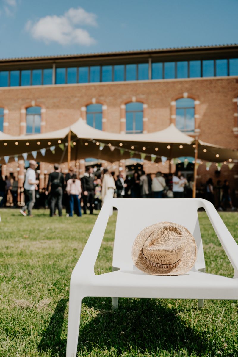 Outdoor event setup with white chairs and string lights against brick building facade.