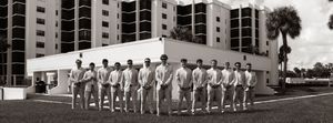 Black and white photo of a groom and groomsmen lined up outdoors near a modern building and palm tree.