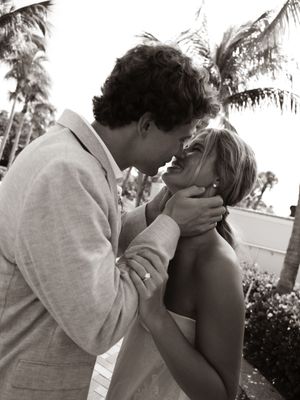Black and white photo of a couple sharing a romantic kiss at a tropical wedding ceremony outdoors.