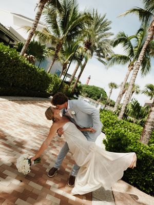 Bride and groom share a romantic dip kiss surrounded by tropical palm trees at an outdoor Florida wedding venue.