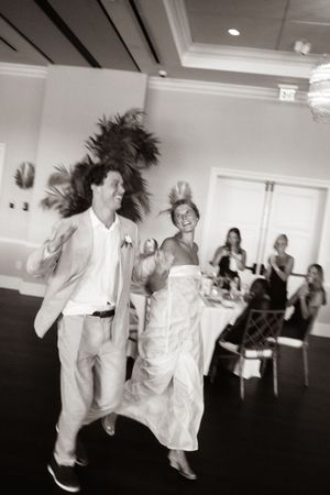 Bride and groom dancing energetically at wedding reception while guests watch in black and white photo.
