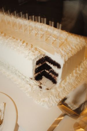 Elegant white wedding sheet cake with candles, revealing dark chocolate layers after being sliced.