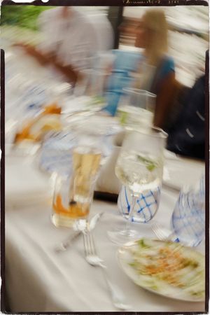 Blurry motion shot of elegant dinner table with champagne flutes, blue glasses, and plates at a formal event.