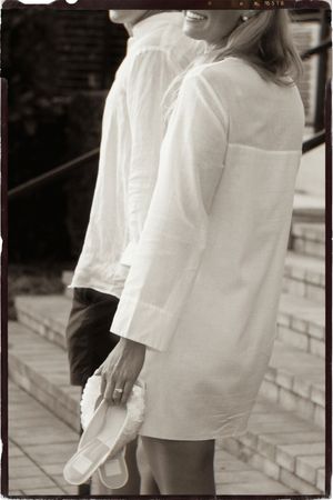 Couple in matching white robes smiling outdoors, woman holding shoes, black and white vintage photo.
