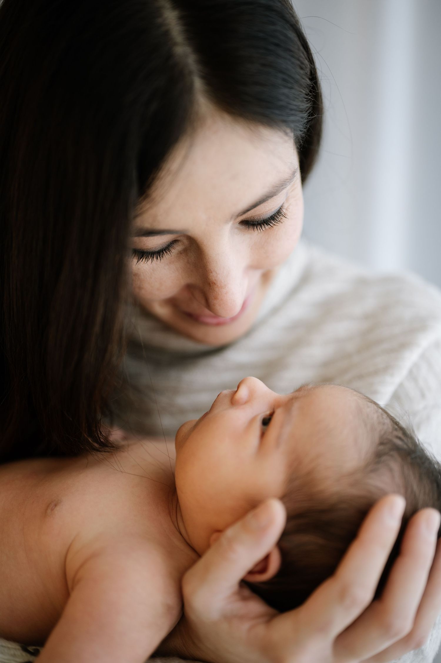 Tender moment between mother and newborn baby in soft window light.