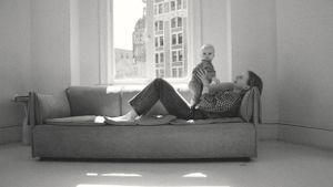 black and white photo of a mom laying on a sofa with her baby boy close to her chest next to a window showing the city behind them.