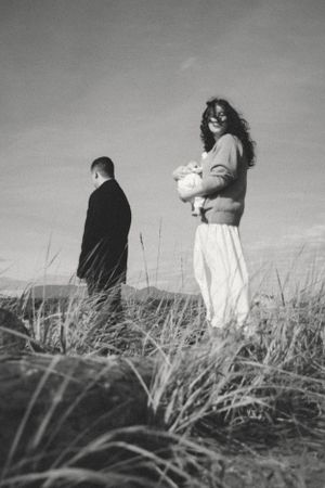 black and white documentary-style newborn outdoor session at Iona Beach in Richmond, BC with the mom holding the baby and looking back
