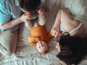 Upside down family portrait shot from above the bed with the baby looking at the camera while the parents play with the baby.