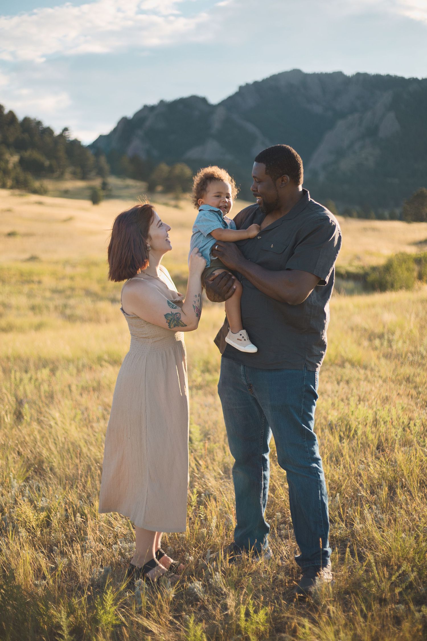 biracial family playing with toddler in large open field boulder flatiron mountains