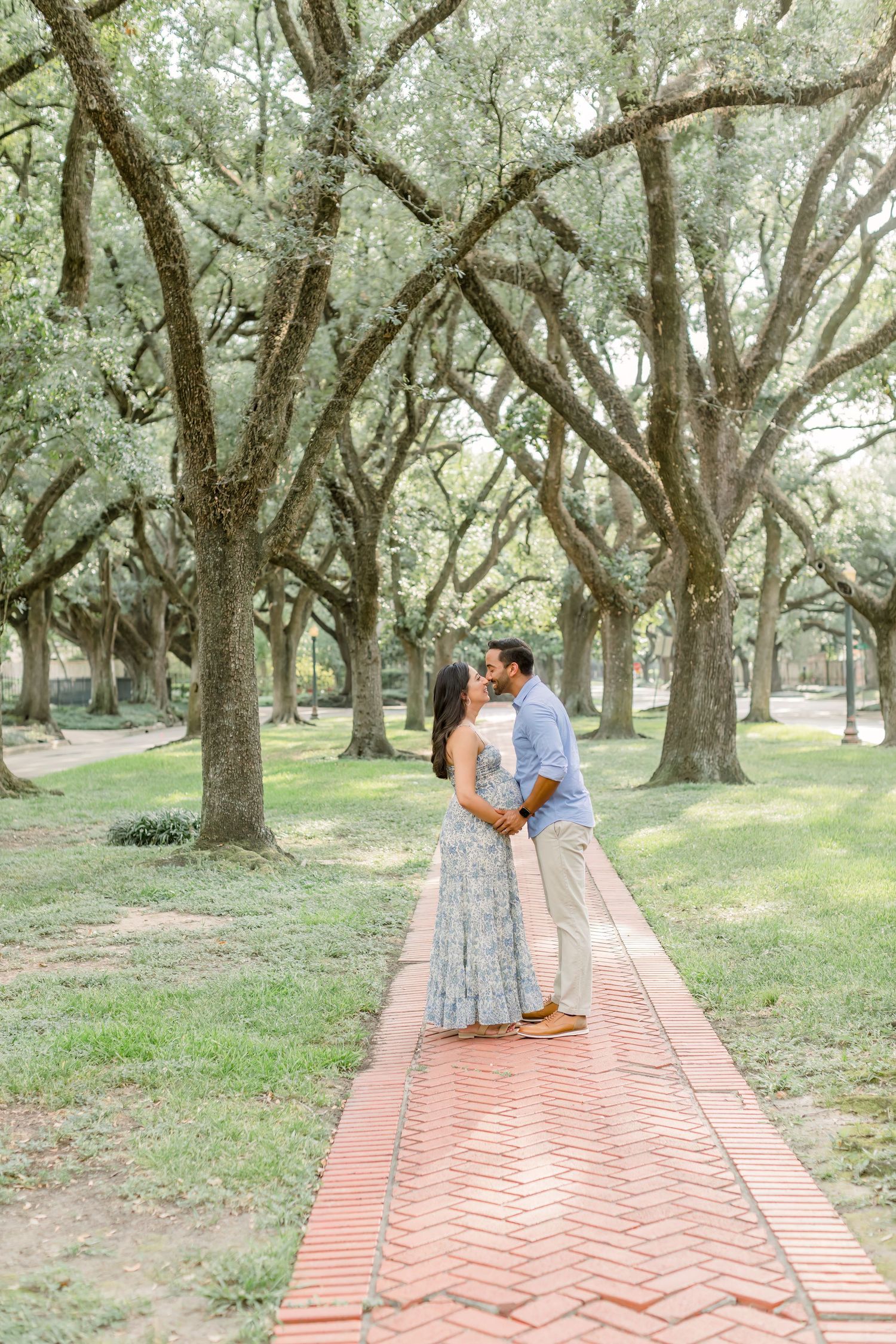 Romantic maternity moment captured on brick walkway beneath Spanish moss-draped trees.