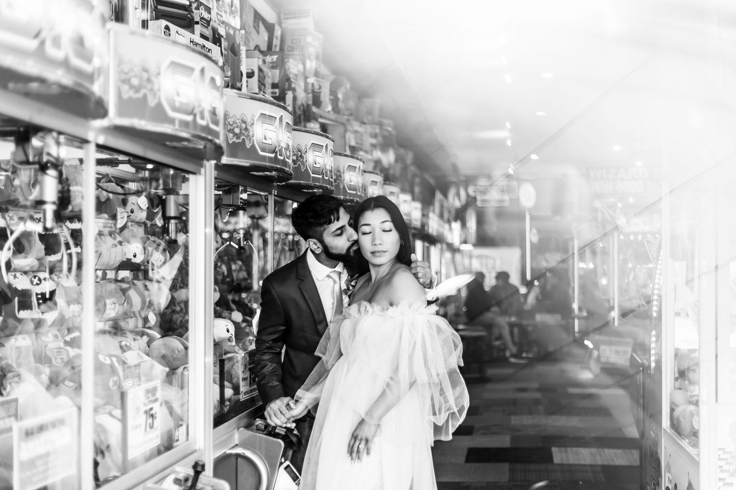 A black and white wedding photo of a couple posing in front of illuminated carnival lights.