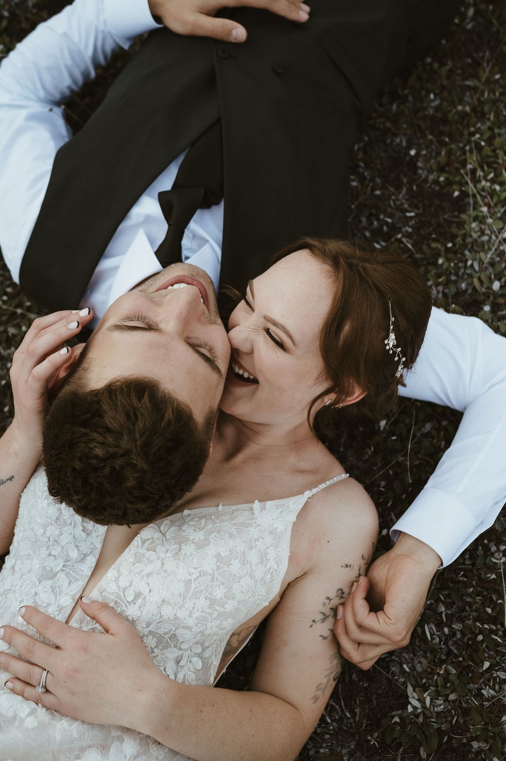 A couple lying on grass laughing together during a wedding photoshoot.
