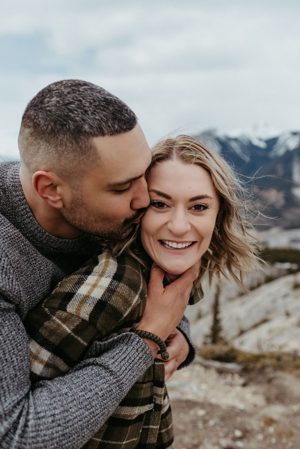 A loving embrace captured against a backdrop of mountain peaks and cloudy skies.