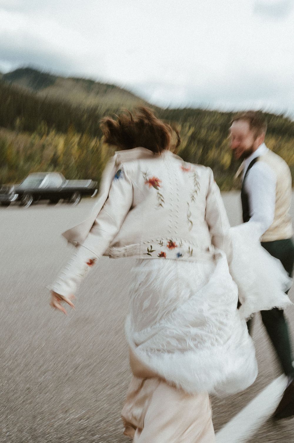A couple in wedding attire dancing on a mountain road with motion blur.