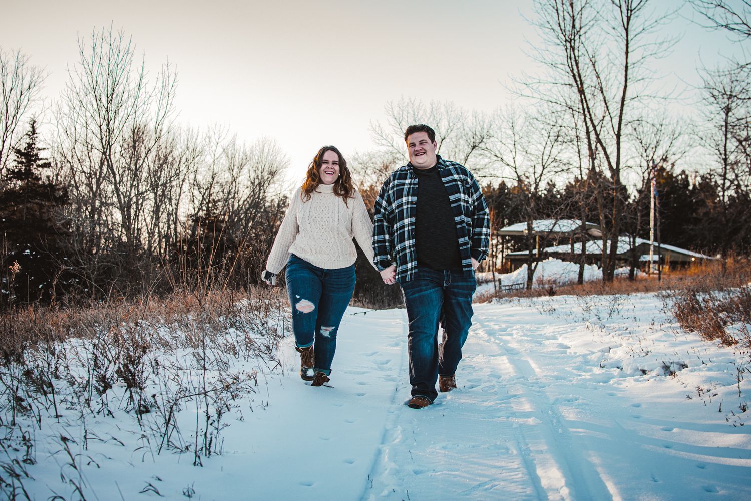 A couple walking hand in hand on a snowy trail during winter surrounded by bare trees.