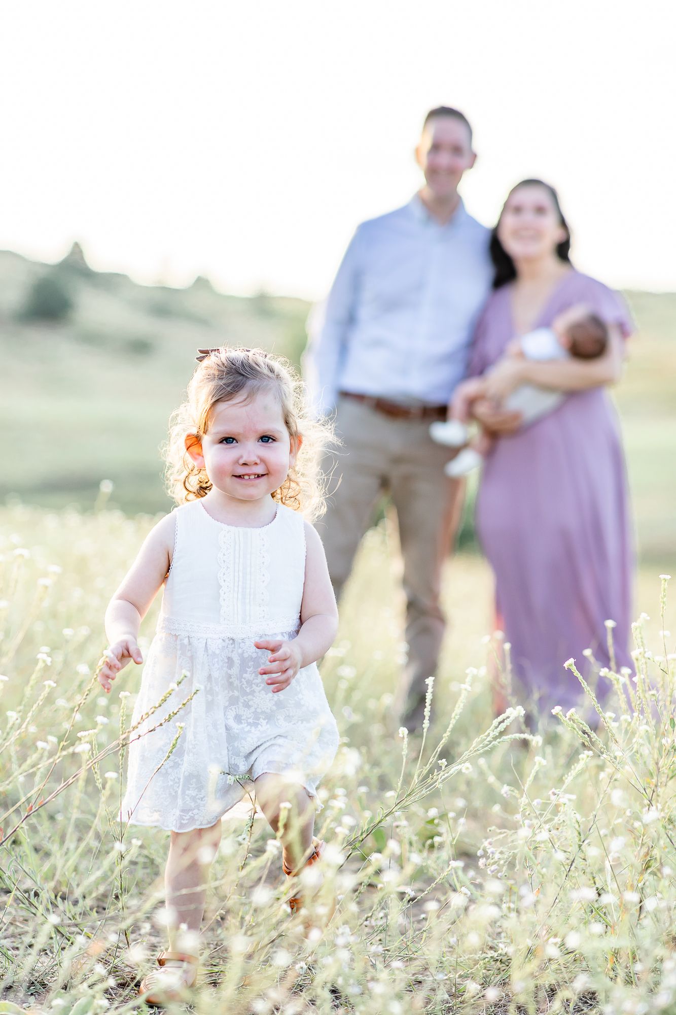 Parents snuggle their new baby boy as their toddler girl wanders toward the camera in Larkspur, Colorado.