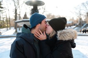 A romantic winter kiss between two people wearing warm hats in the snow.