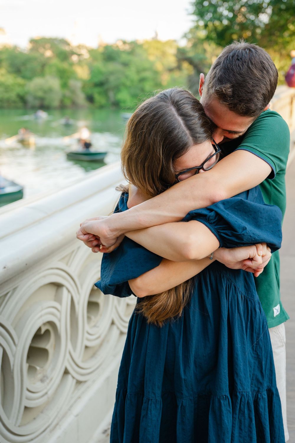 A tender embrace shared between a couple on a bridge overlooking a lake during sunset.