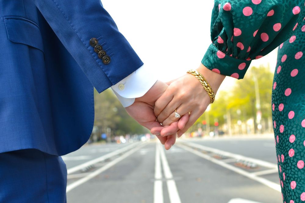Two people holding hands while walking down a street, one in blue suit and one in polka dot dress.