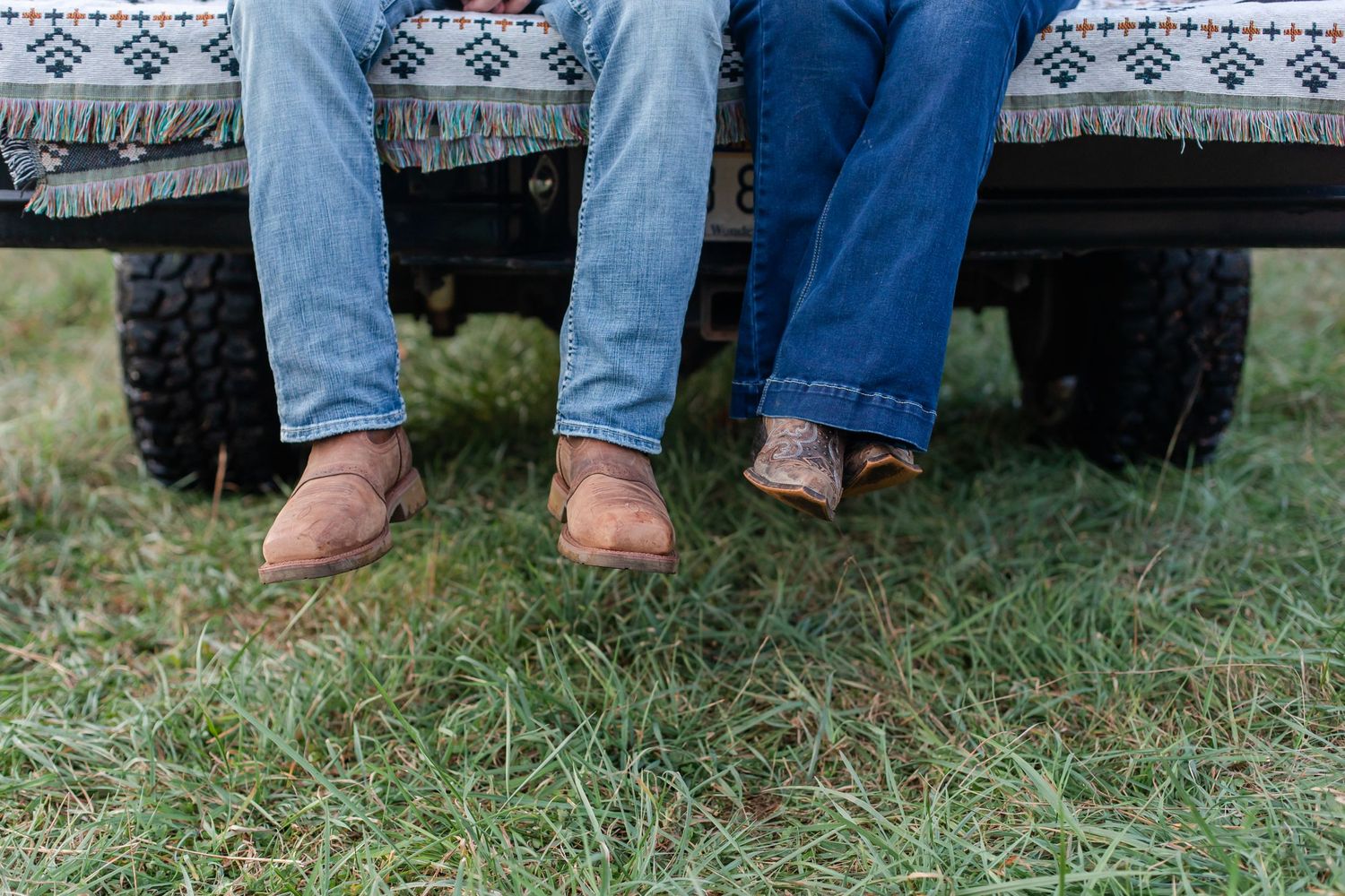 Casual feet and legs sitting on grass with southwestern pattern blanket visible.