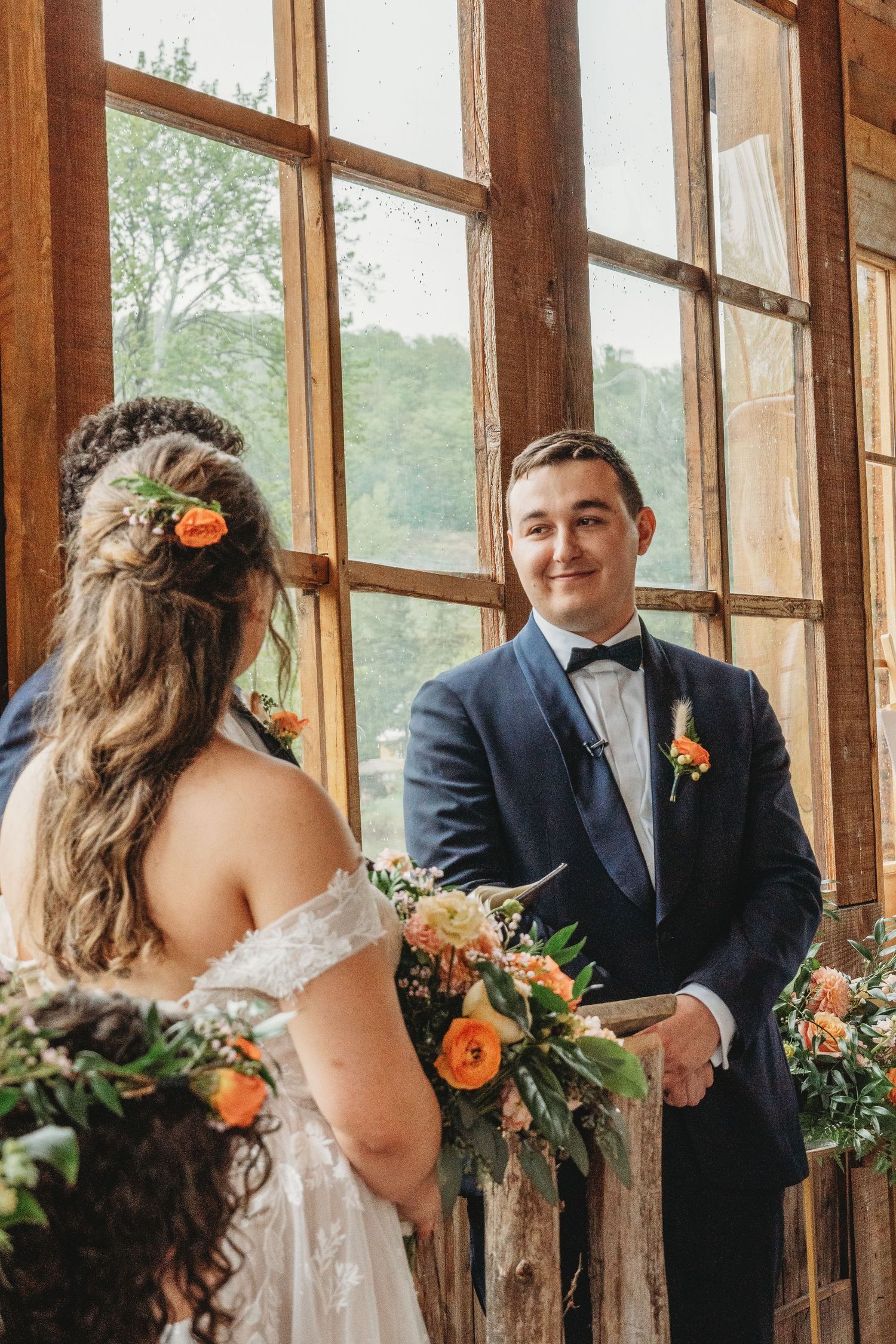 Exchange of vows near large windows in rustic venue with coral floral accents.