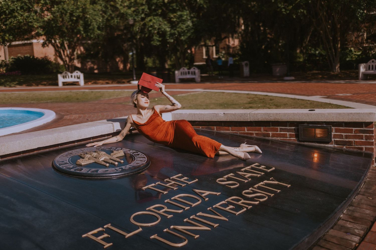 A person in orange leaning over a Florida State University seal on the ground near a pool.