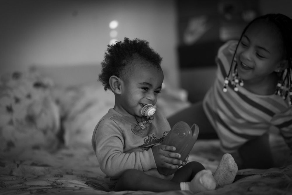 A tender moment captured in black and white as a child enjoys playtime on a bed.