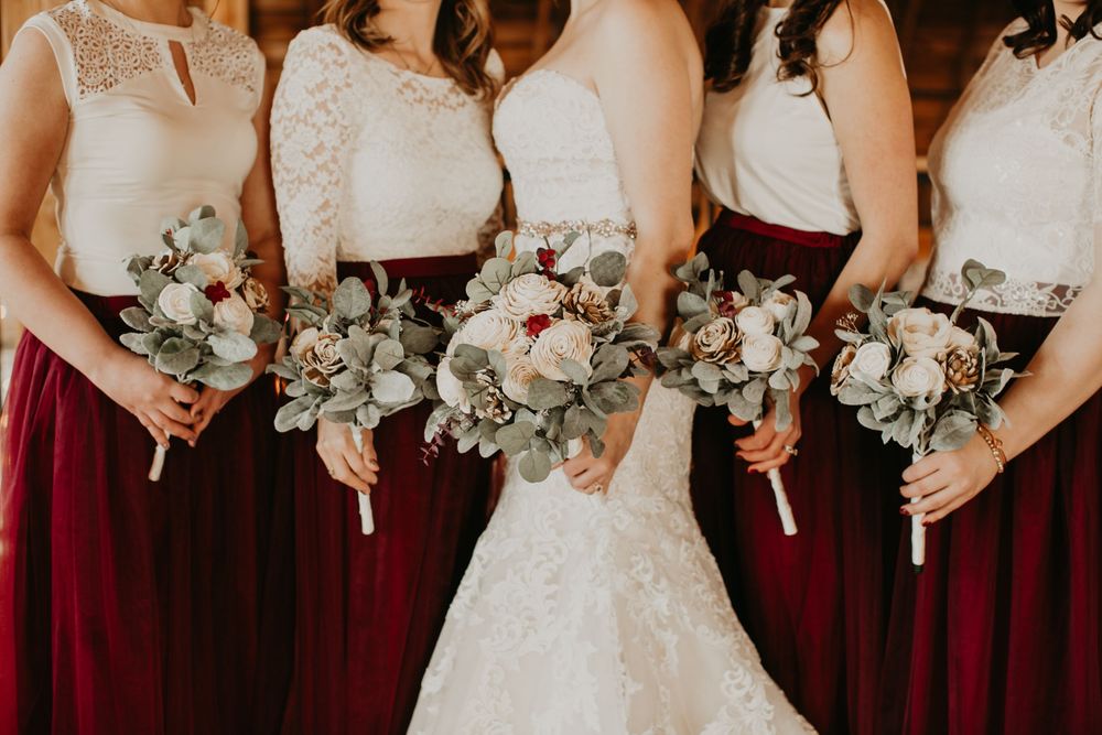 Bride and bridesmaids in burgundy skirts display elegant eucalyptus and rose wedding bouquets.