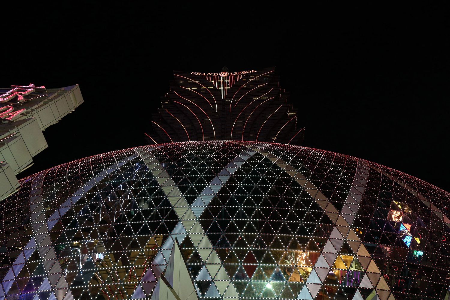 Illuminated geometric dome structure of Grand Lisboa casino in Macau against dark night sky.