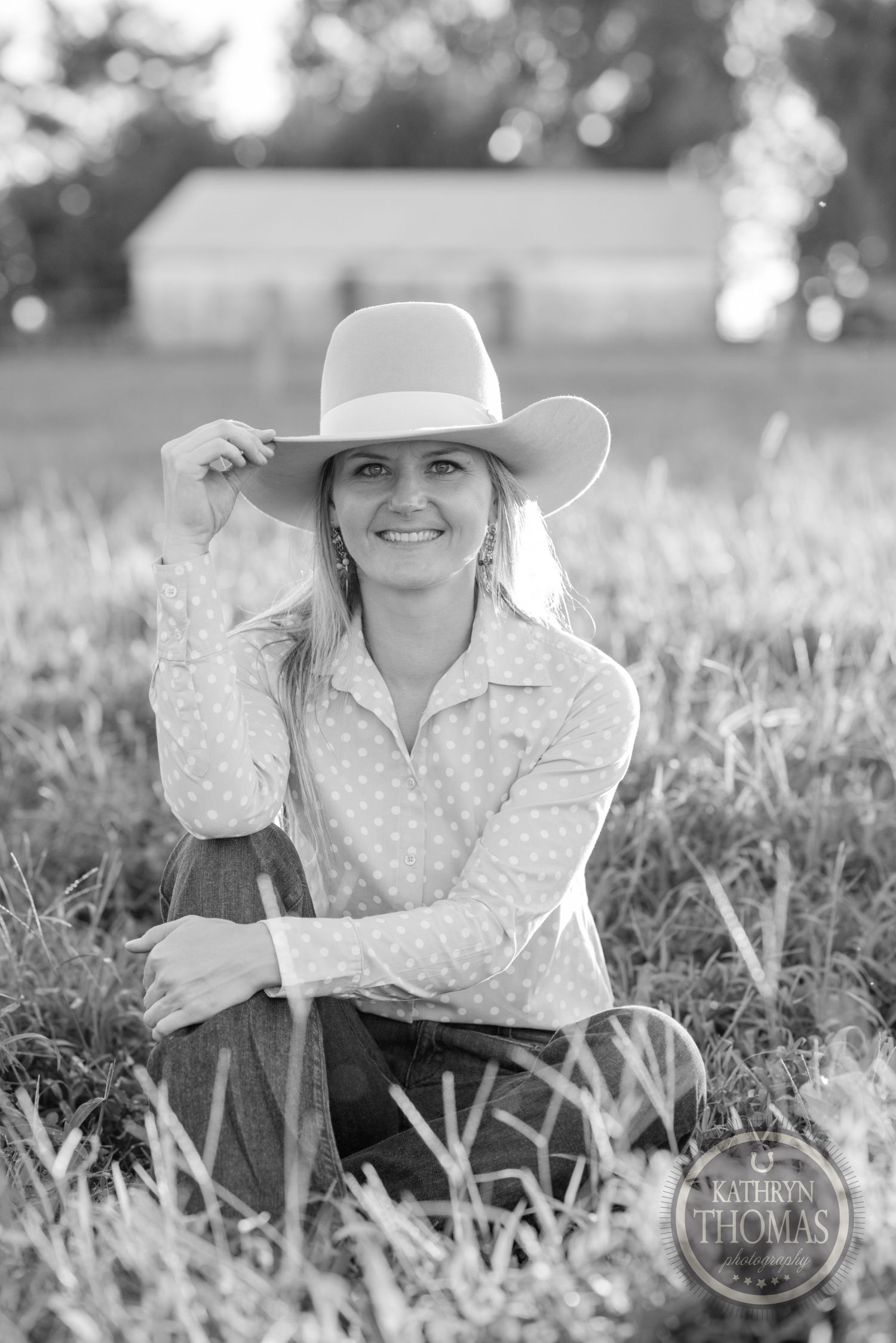 A black and white portrait shows someone in western attire sitting in a rural field.