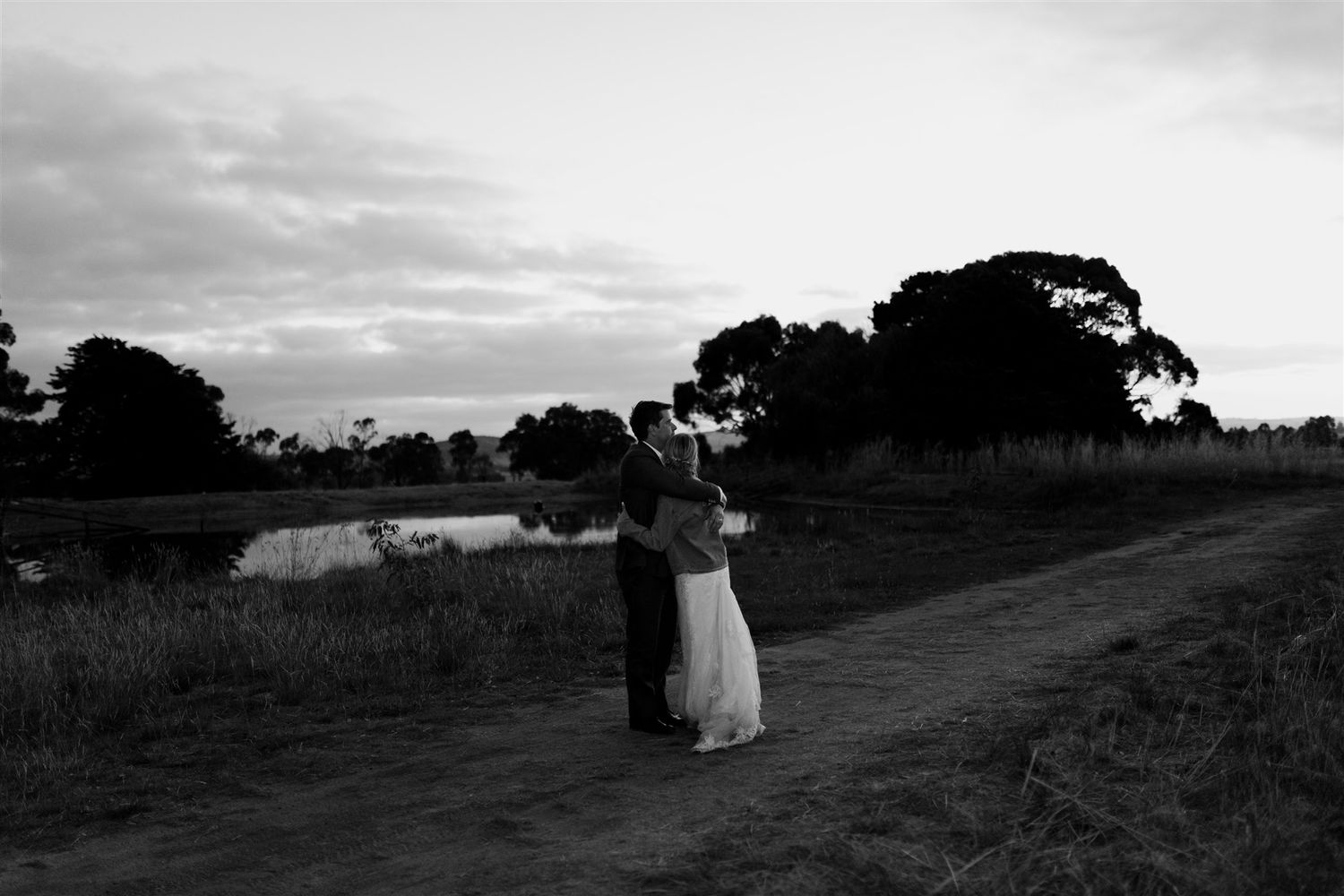 A couple embraces on a country path at sunset in black and white.