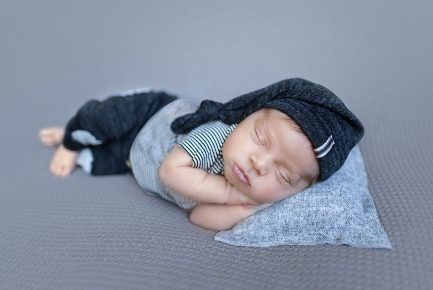 Peaceful sleeping infant wearing navy outfit on grey textured backdrop.