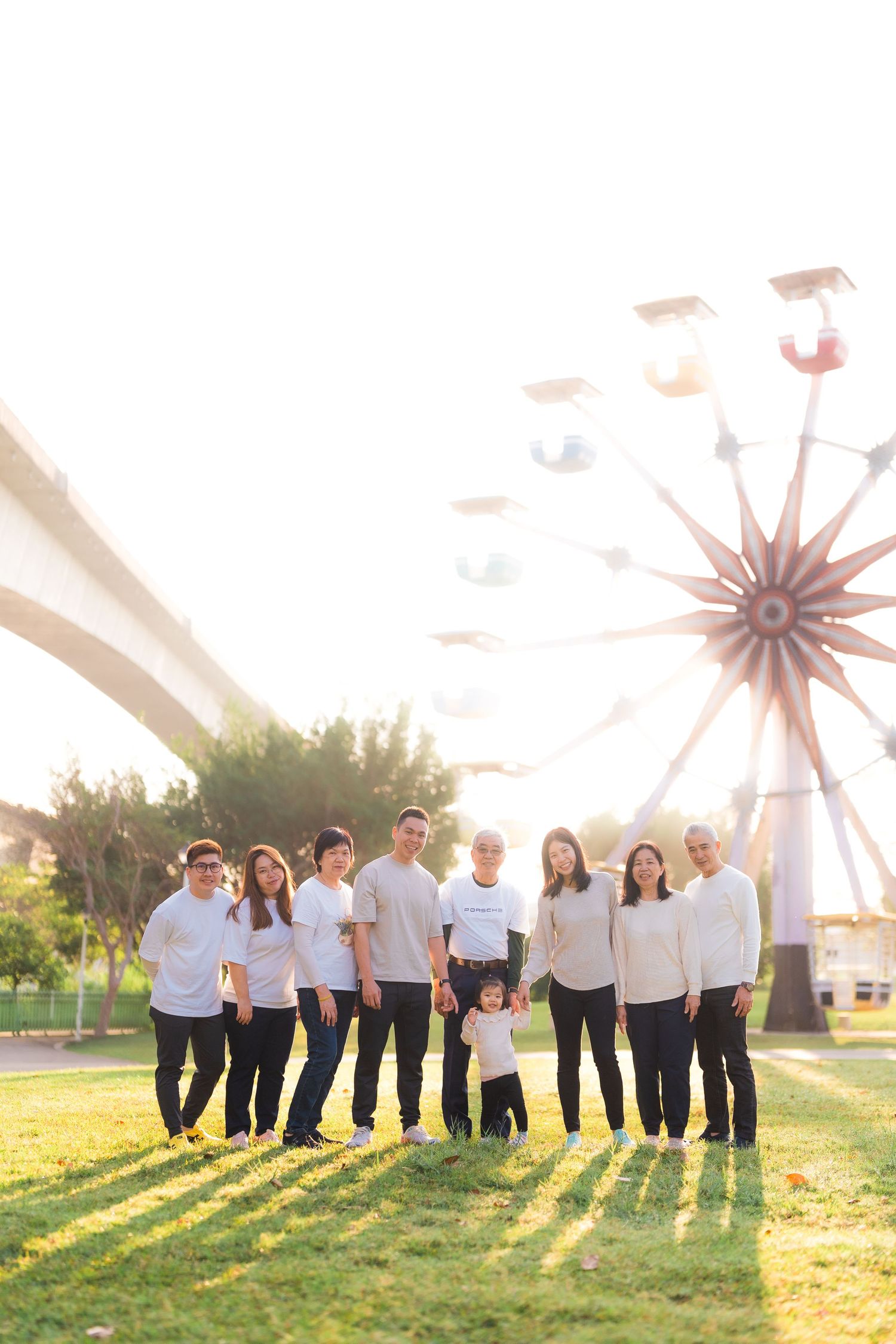 Group wearing matching white outfits poses in front of ferris wheel at sunset.