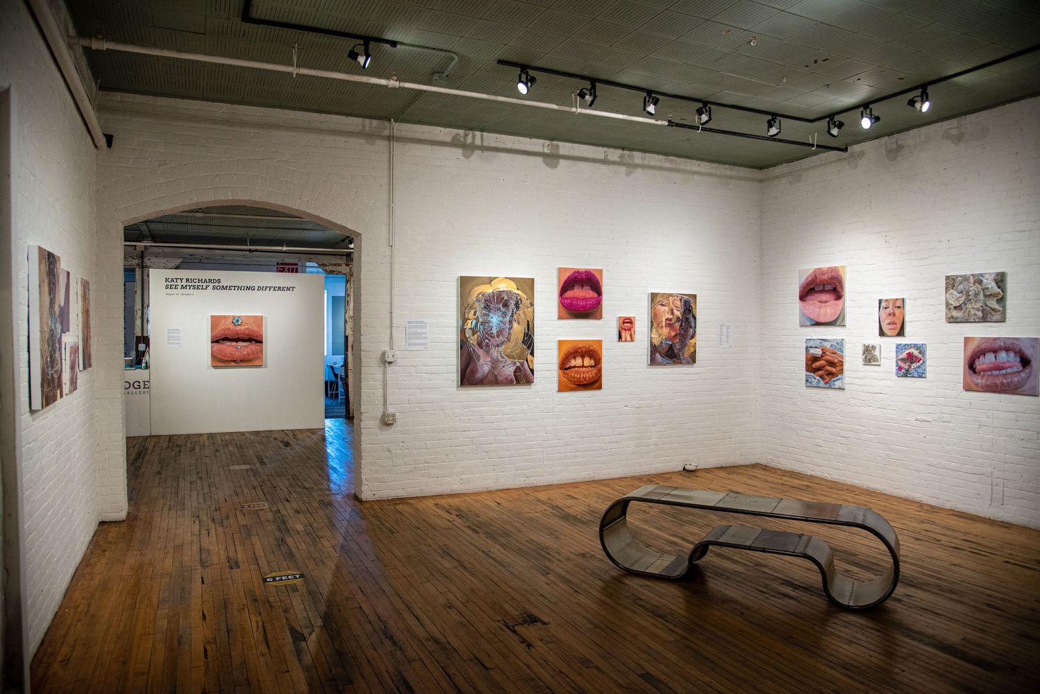 Art gallery interior with white walls displaying framed artwork and wooden flooring.