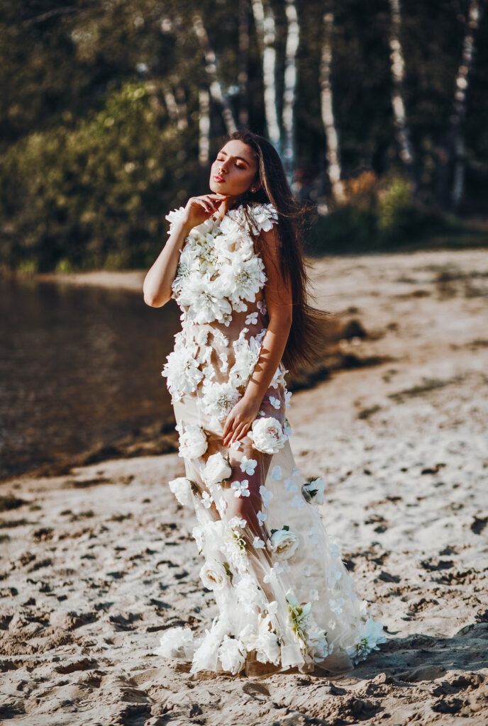 Ethereal white floral dress with flowing design photographed against birch trees and sandy beach at sunset.