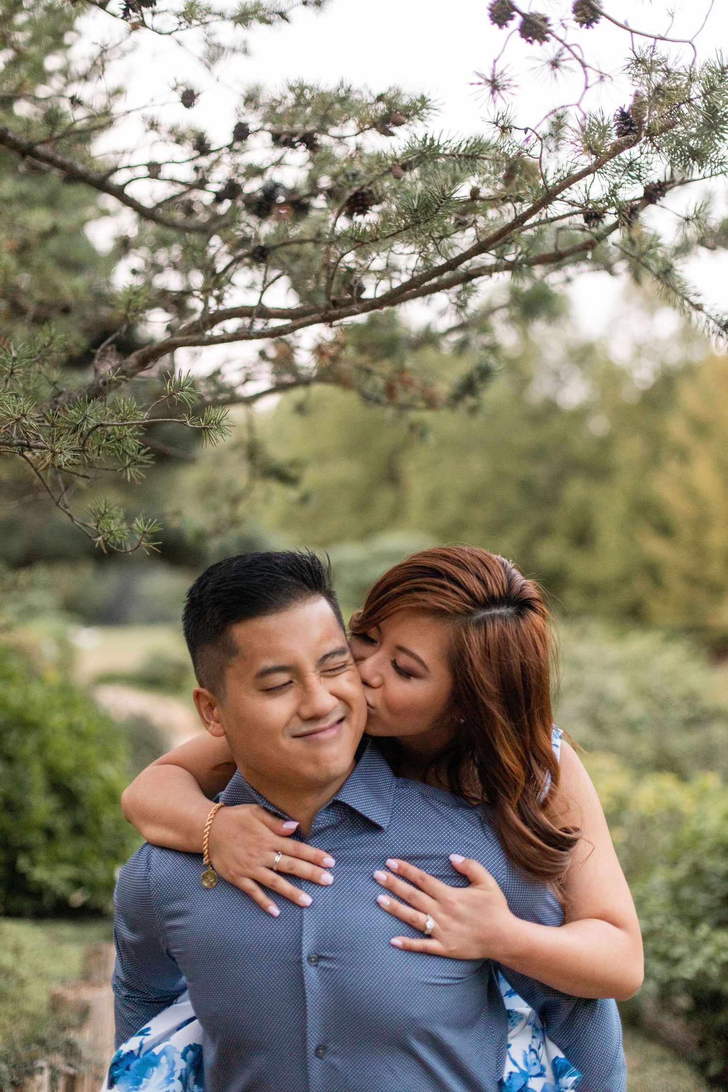 Couple embraces in casual outdoor setting with natural greenery.