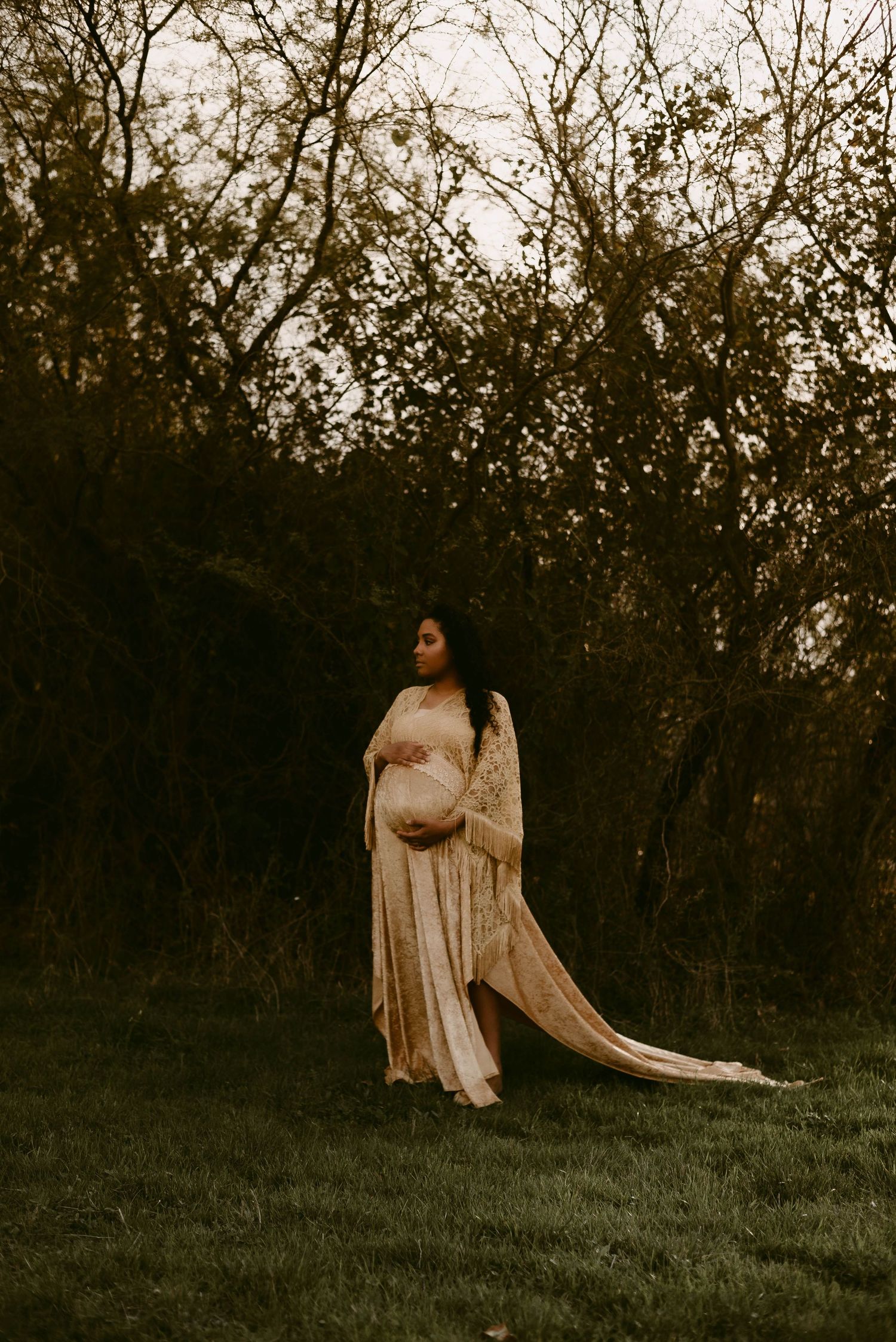 Dreamy silhouette maternity photo with long lace shawl against dusky wooded background.