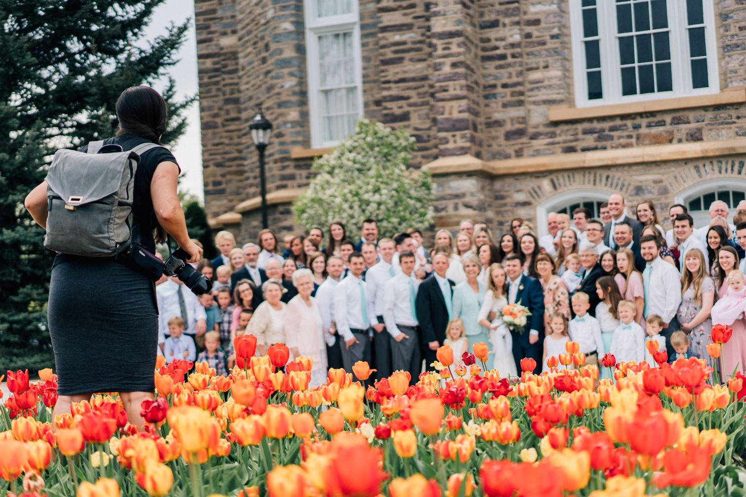 Photographer captures large wedding group behind vibrant orange and red tulip garden.