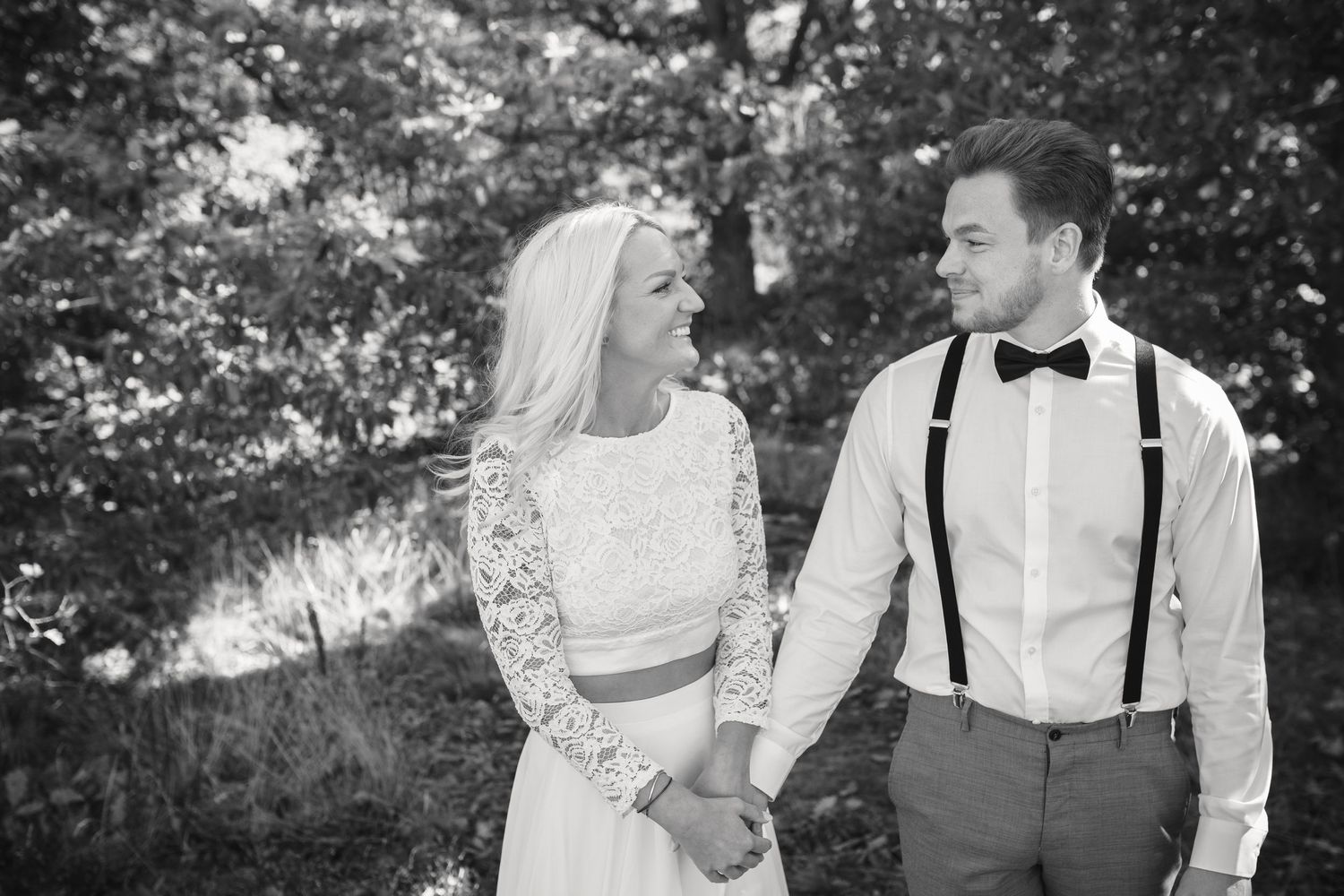 A black and white portrait of a bride and groom sharing a romantic moment in a wooded setting.