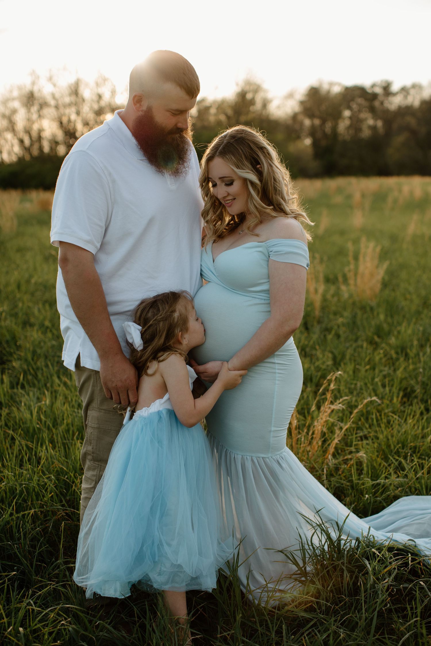 Family portrait in field with child wearing matching light blue dresses at sunset.
