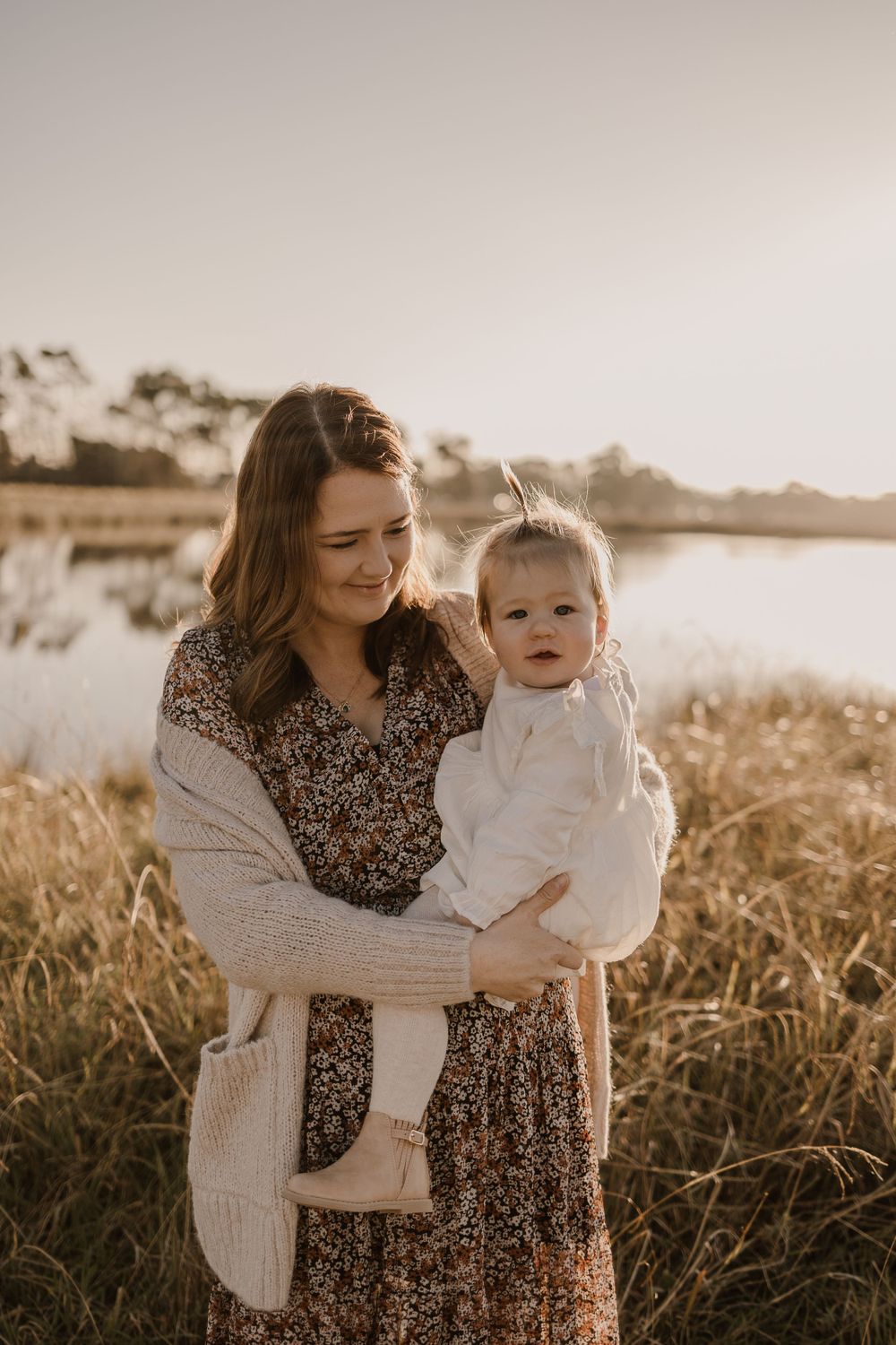 A tender moment between parent and child by a lake at sunset.