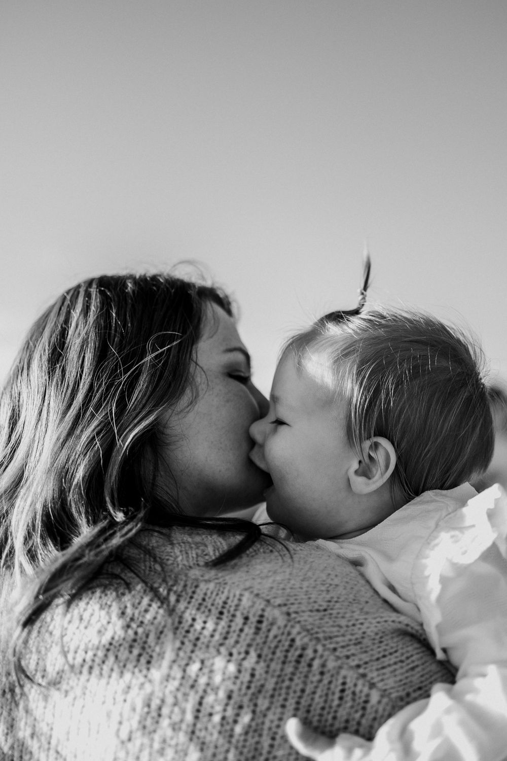 Intimate black and white photograph of parent and baby sharing a loving kiss.