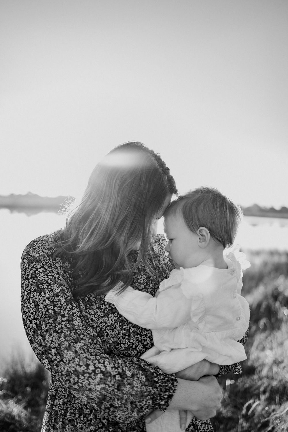 Black and white photograph showing tender moment between parent and child near water.