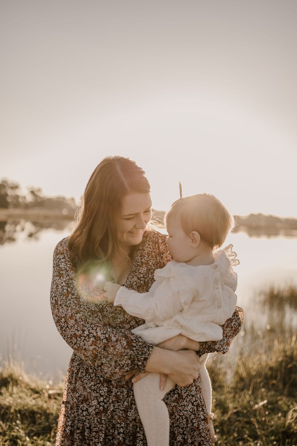Sunlit portrait showing joyful interaction between parent and baby outdoors.