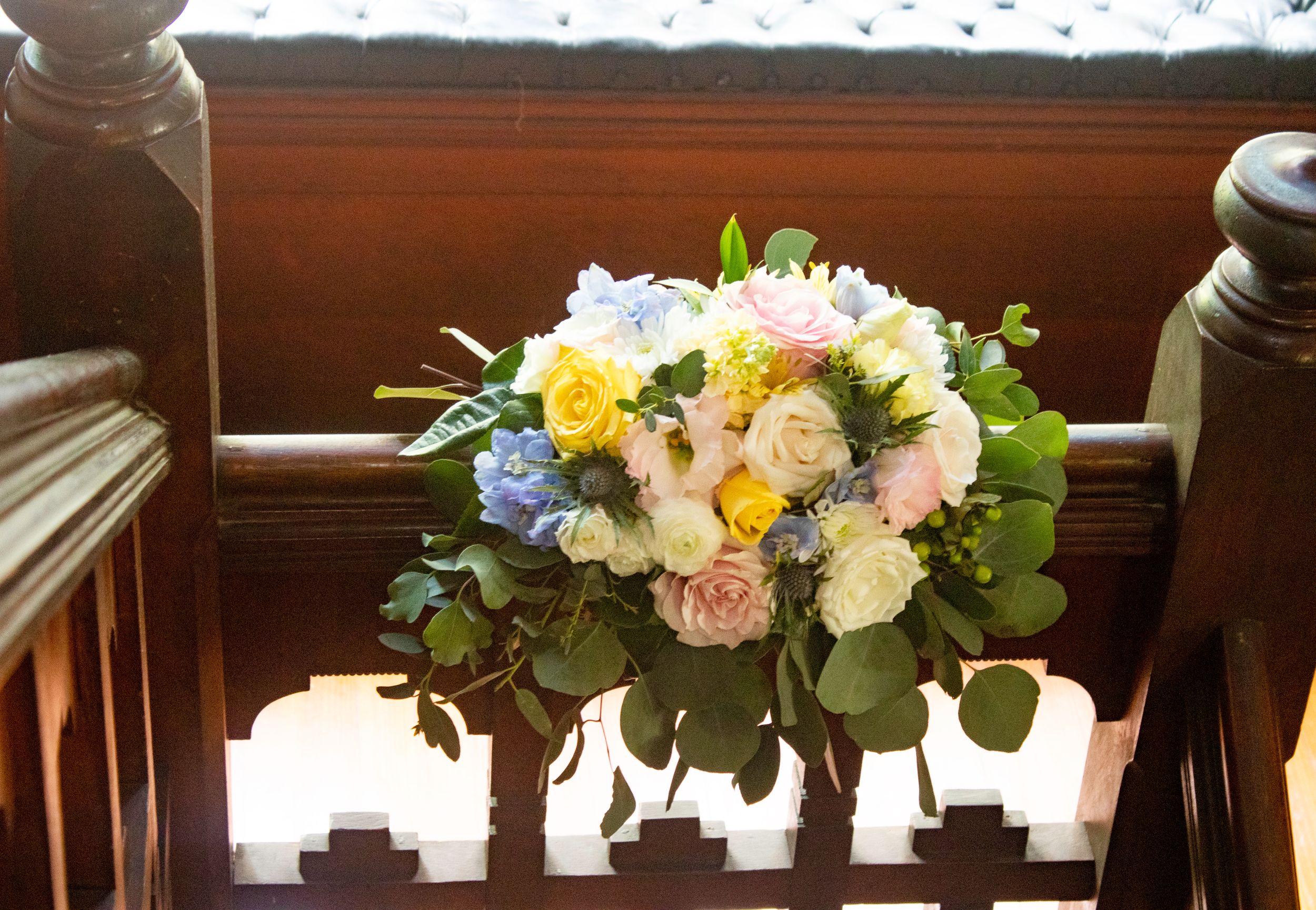 A collection of elegant floral centerpieces with white and yellow blooms arranged in vases along a wooden surface.