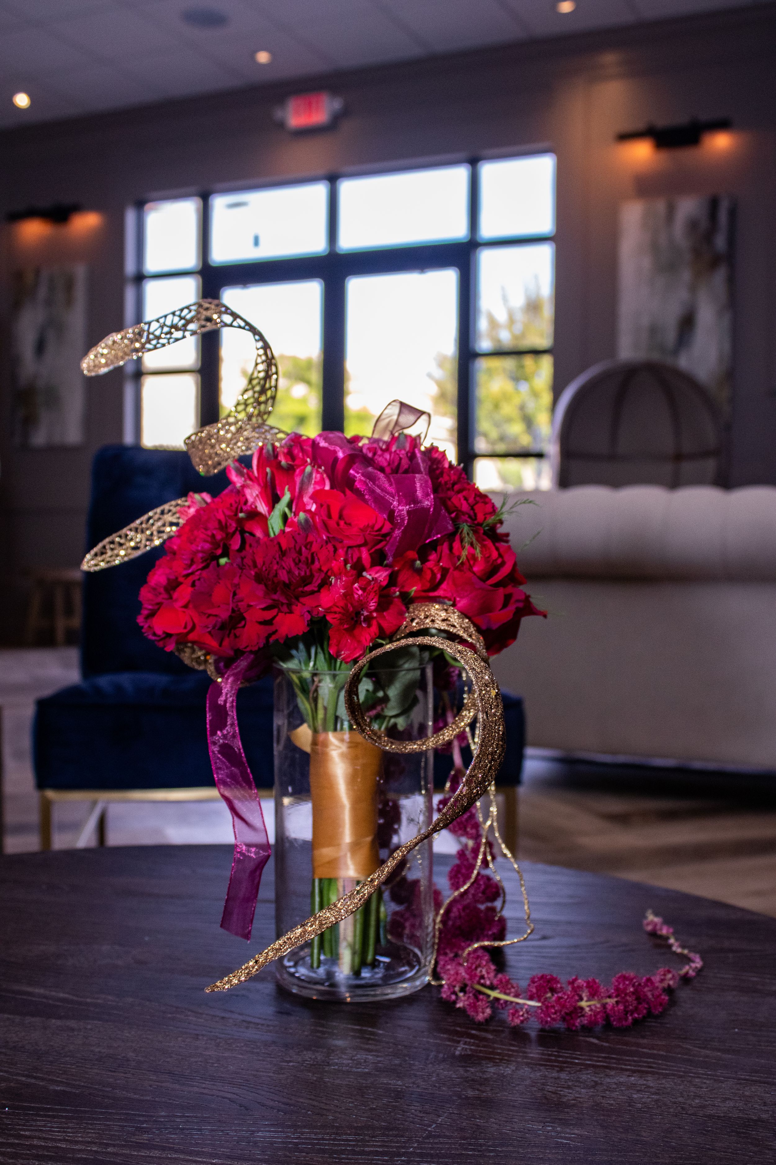 Red carnation floral centerpieces with gold accents arranged on dark wooden tables in an elegant event space.