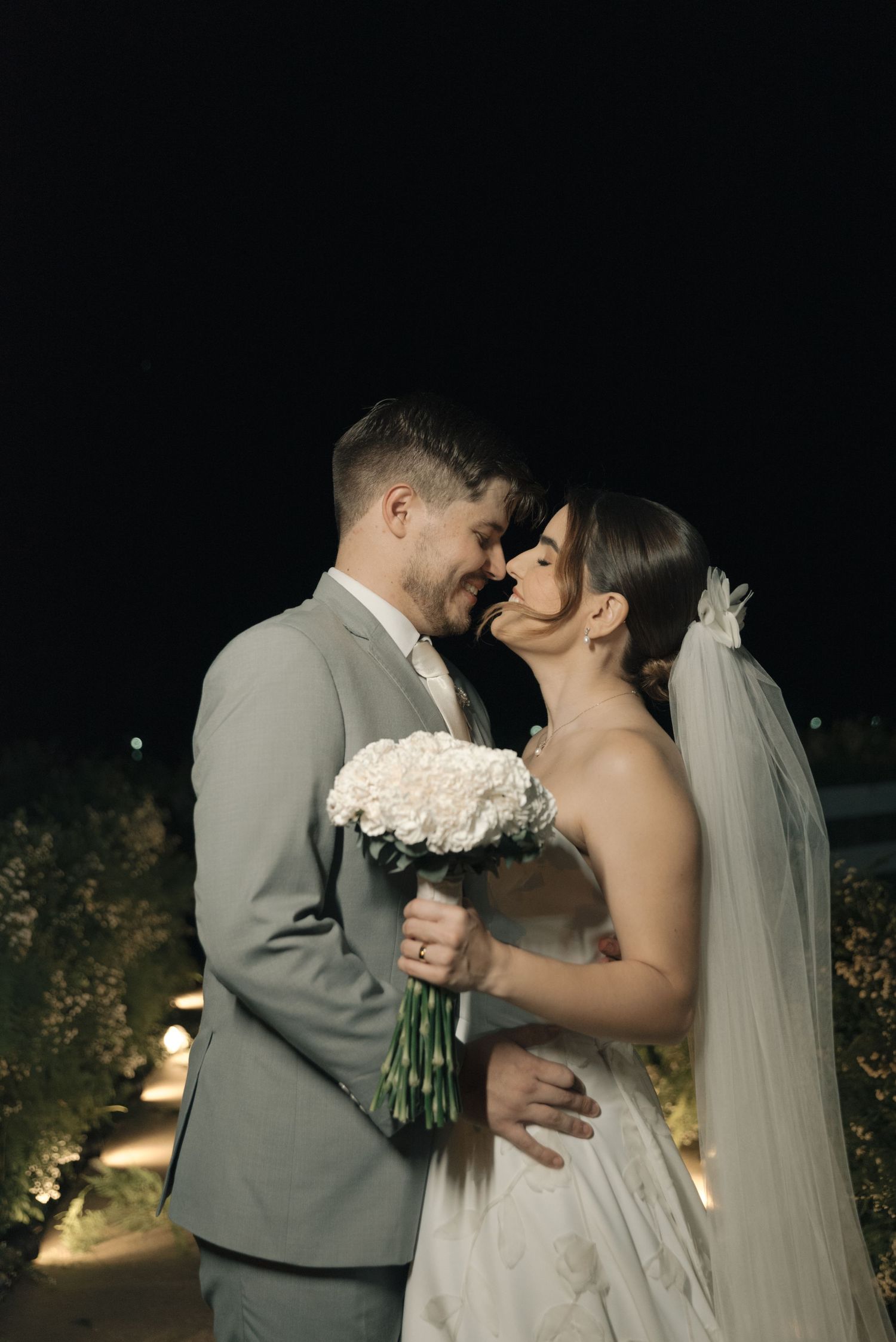 Romantic nighttime wedding portrait with couple sharing tender moment and white bouquet.