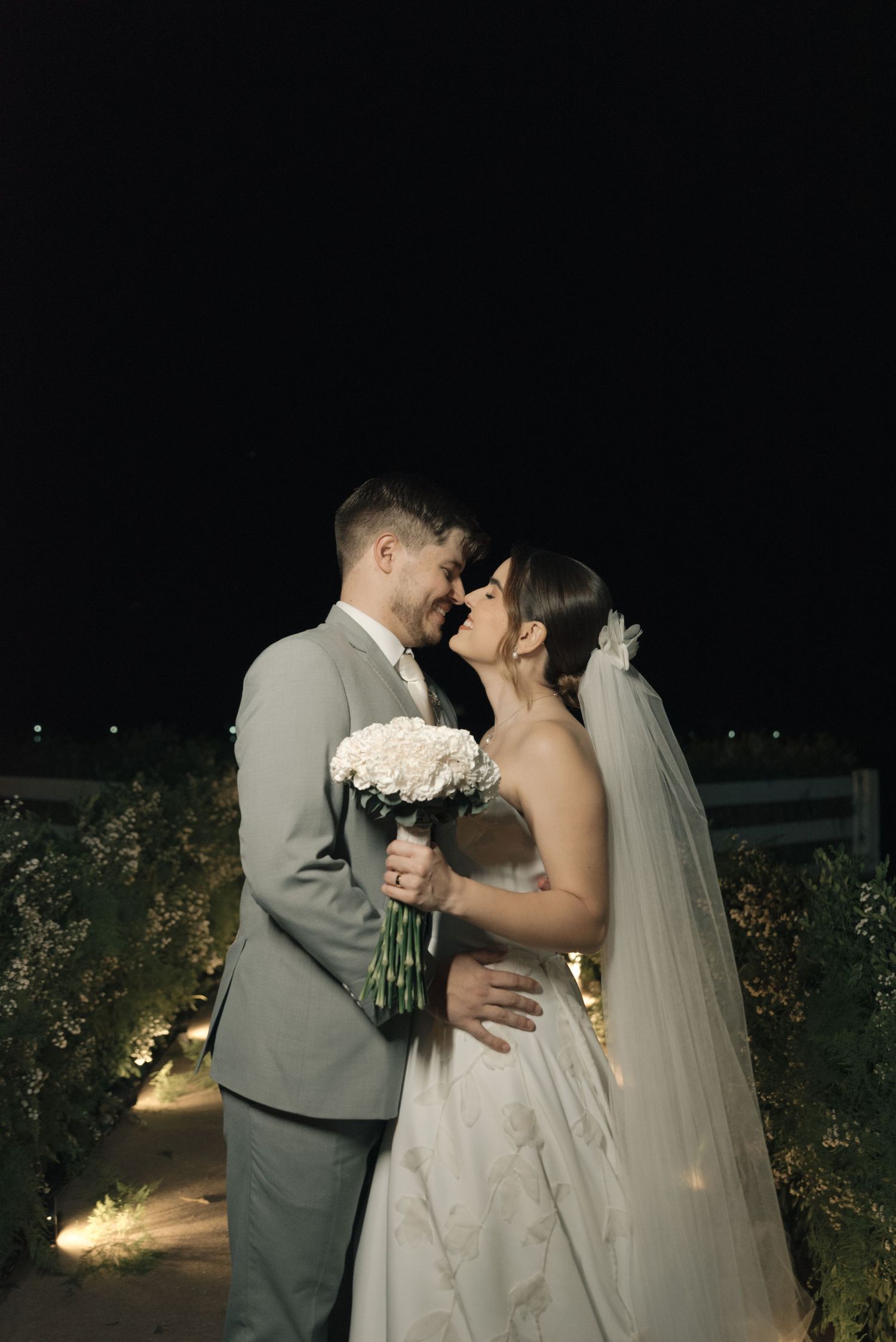 Intimate nighttime wedding portrait with couple laughing and holding white flowers.