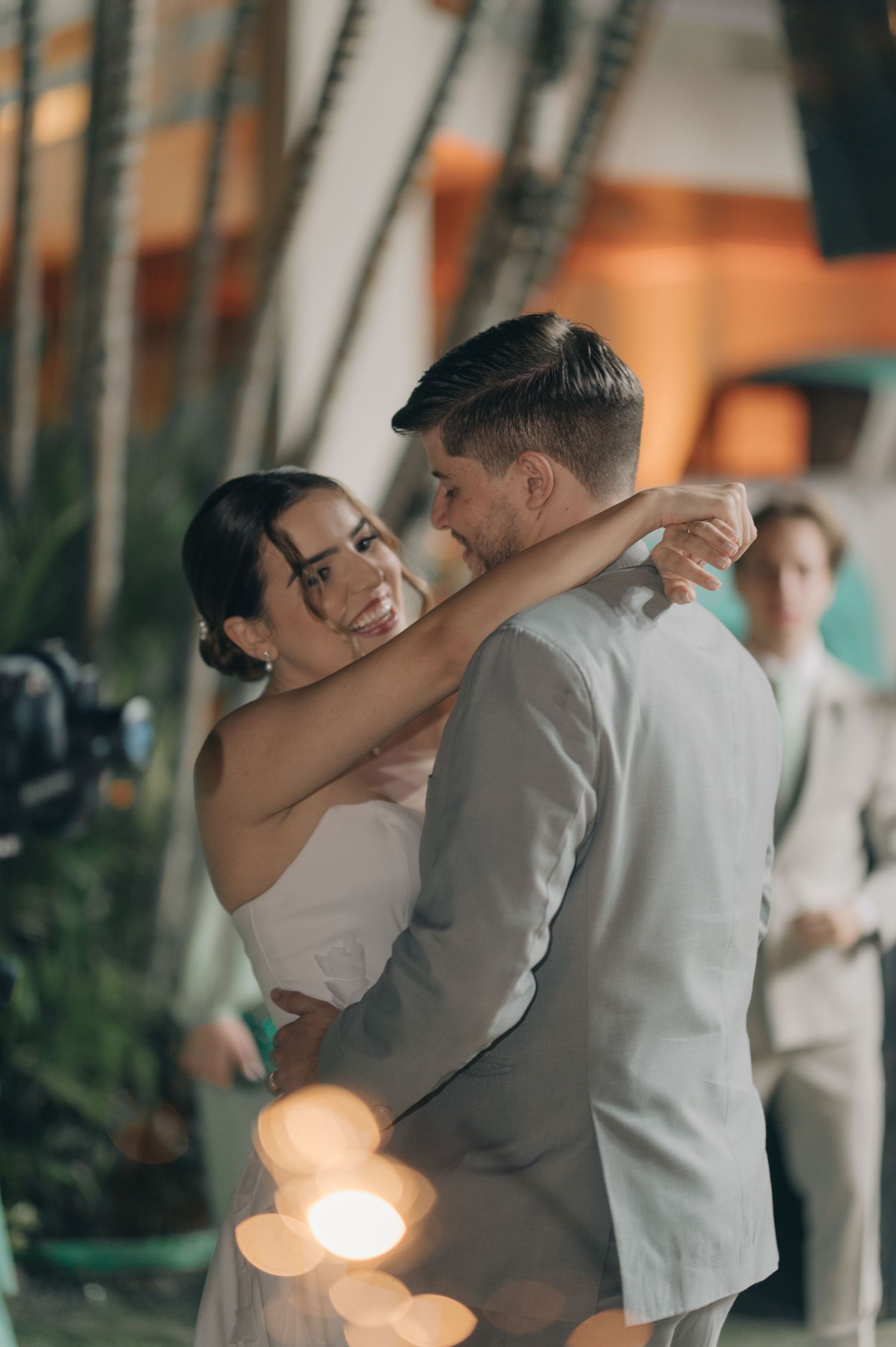 Couple sharing first dance with soft lighting and tropical plants in background.