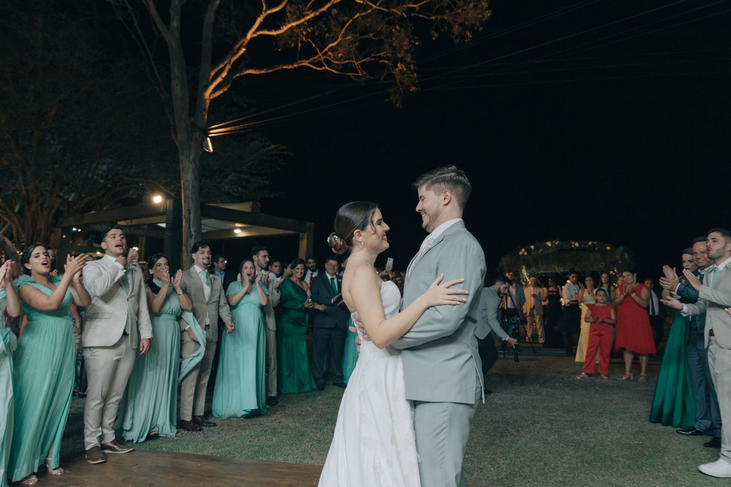 Wedding couple shares dance on outdoor reception floor surrounded by guests in mint green dresses.